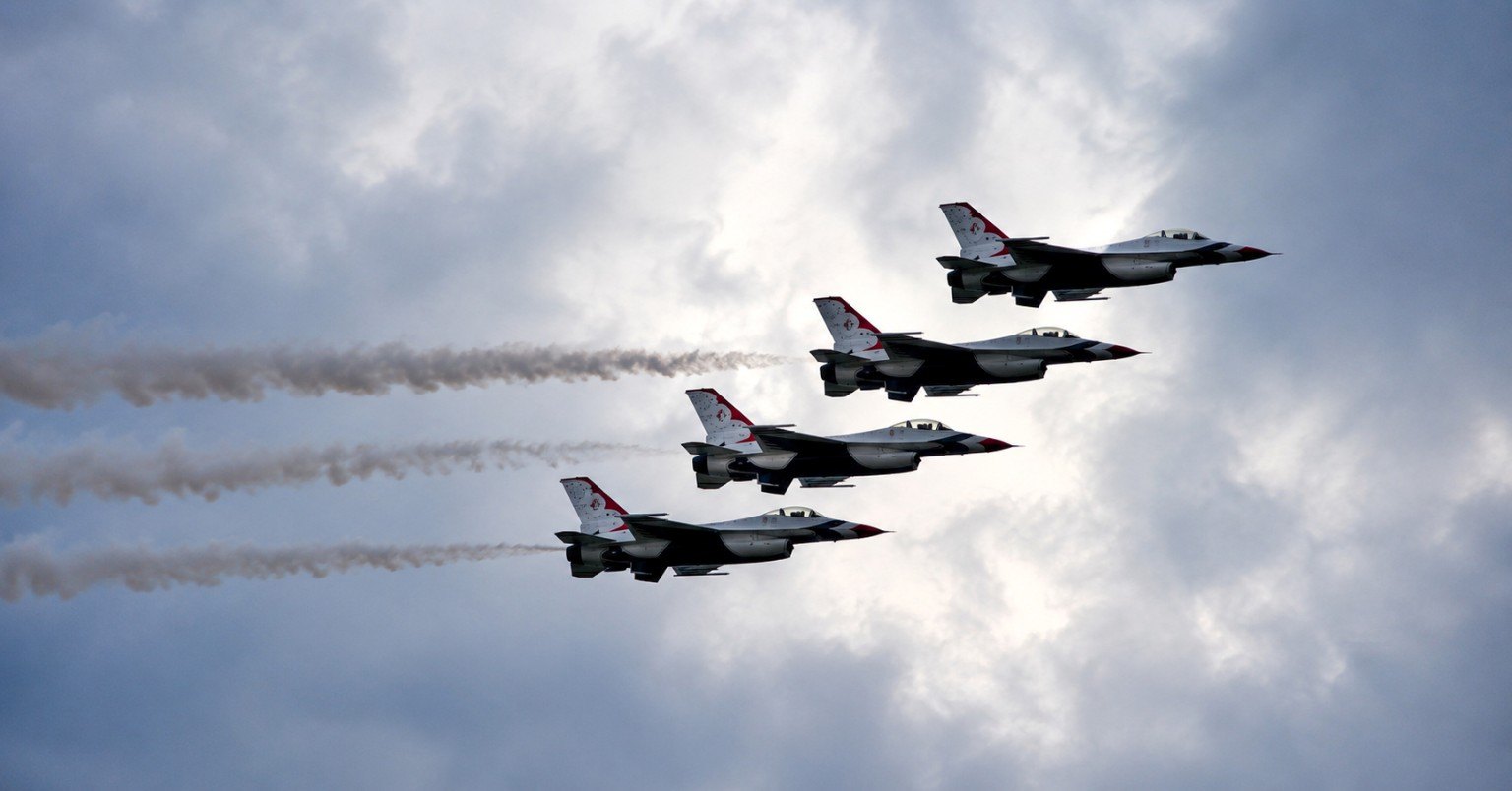 Four Thunderbirds aircraft flying in tight formation across a cloudy sky.